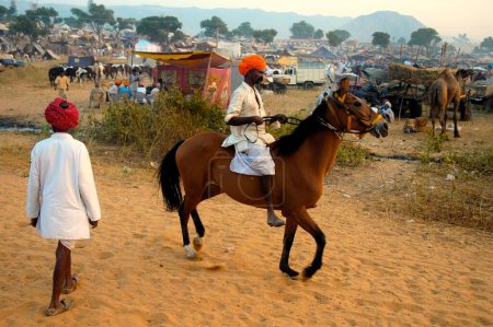 Foto de Caballo comerciante paseos a caballo en la feria de ganado de Pushkar; Pushkar; Rajastán; India - Imagen libre de derechos