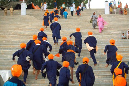 Foto de Grupo de jóvenes sikh vestidos de azul con accesorios de cabeza de azafrán subiendo escaleras de Sachkhand Saheb Gurudwara, 300º año de Consagración de Guru-Granth Sahib en Nanded, Maharashtra, India 30-October-2008 - Imagen libre de derechos