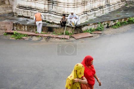 Foto de Dos mujeres rurales indias que pasan por la carretera cerca de un antiguo templo de Jain; Village Delwara; Udaipur; Rajasthan; India - Imagen libre de derechos