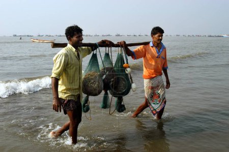 Foto de Pescadores indios del sur de Asia llevando cargas de pescado de su barco anclado en el mar para la venta en Uttan Beach; cerca de Bombay ahora Mumbai; Maharashtra; India - Imagen libre de derechos