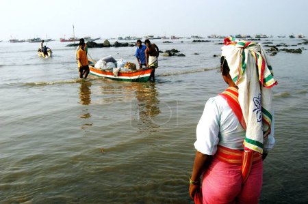 Foto de Pescadoras indias del sur de Asia esperando que los peces sean llevados a la playa en botes más pequeños para ser vendidos en el mercado local en Uttan Beach; cerca de Bombay; ahora Mumbai; Maharashtra; India - Imagen libre de derechos