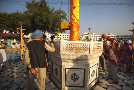 Photo for Sikh devotee paying his respect to Nishansahib (holy flag of Sikhs draped in saffron robes) in compound of Sachkhand Saheb Gurudwara, Nanded, Maharashtra, India - Royalty Free Image