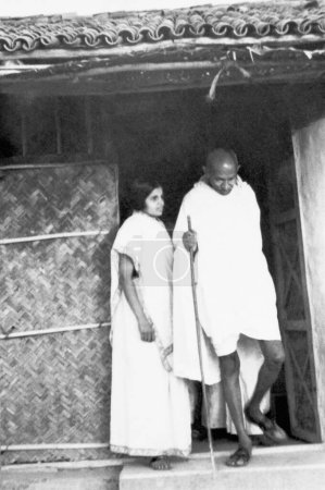 Téléchargez les photos : Mahatma Gandhi, accompagné de la coashramite Chandan Kalelkar, quittant sa cabane à l'Ashram de Sevagram, 1940 - en image libre de droit