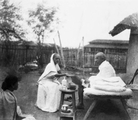 Téléchargez les photos : Kasturba Gandhi et Mahatma Gandhi petit déjeuner devant la cabane du Mahatma Gandhis à l'Ashram de Sevagram, 1940 - en image libre de droit