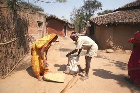 Téléchargez les photos : Dame achetant du grain à un marchand traditionnel en échange de vieilles choses dans un village du Jharkhand, en Inde - en image libre de droit