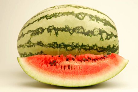 Photo for Fruits ; One full watermelon with light and dark green stripes and one cut slice showing red watery pulp with black seeds ; Pune ;  Maharashtra ; India - Royalty Free Image