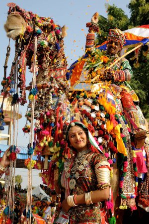 Photo for Girl in traditional jewellery and rajasthani costume standing in front of decorated camel in Pushkar fair, Rajasthan, India - Royalty Free Image