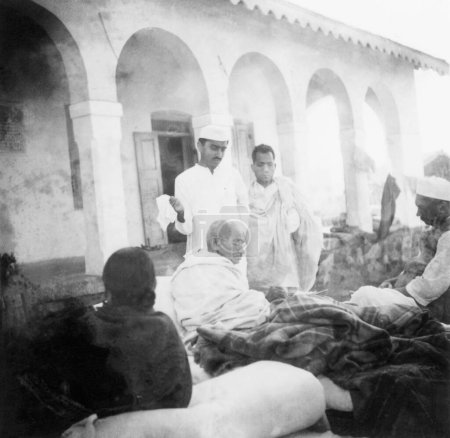 Foto de Mahatma Gandhi sentado frente al edificio principal en Rashtriyashala Ashram, Rajkot, durante su ayuno, 1939 de Purushottam Gandhi, Brijkrishna Chandiwalla y Mathurdas Trikamji, India - Imagen libre de derechos