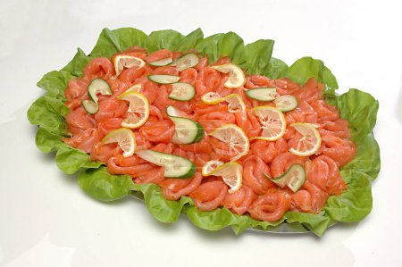Non vegetarian Food , Fish Smoked Salmon (Rokt Lax in Swedish) surface texture clean and bone less , slices arranged in folded shapes and topped with lemon and cucumber thin and twisted slices