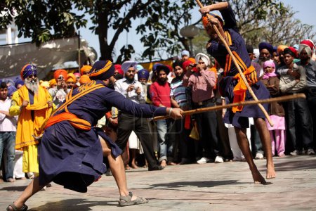 Téléchargez les photos : Guerriers nihang ou sikhs effectuant des cascades avec des bâtons de bois lors des célébrations Hola Mohalla à Anandpur sahib dans le district de Rupnagar. Punjab. Inde - en image libre de droit