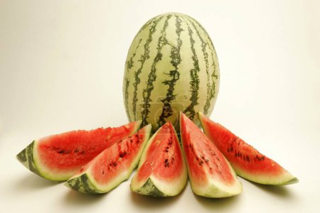 Photo for Fruits ; One full watermelon with light and dark green stripes with five cut slices showing watery red pulp and black seeds ; Pune ; Maharashtra ; India - Royalty Free Image