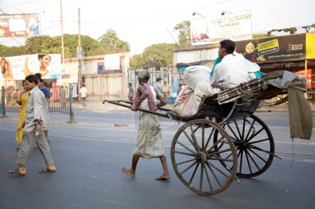 Foto de Escena callejera, tirador de rickshaw mano tirando con el pasajero en la carretera, Calcuta ahora Kolkata, Bengala Occidental, India - Imagen libre de derechos