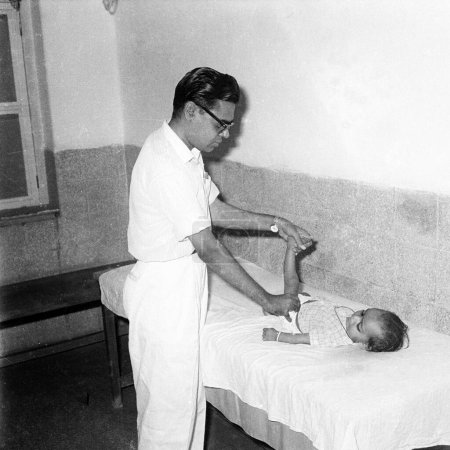 Téléchargez les photos : Vieux millésime 1900 noir et blanc image de médecin indien vérifier bébé Inde Années 1940 - en image libre de droit