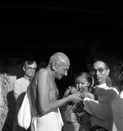 Foto de Mahatma Gandhi presenta un regalo de cumpleaños a Nandini, sobrina de su secretario Pyarelal Nayar (derecha) en Sevagram Ashram, Vardha, Maharashtra, India, agosto 1944 - Imagen libre de derechos