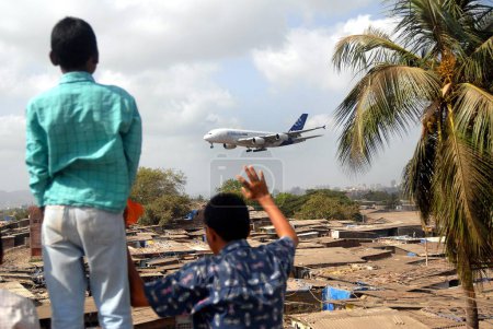 Téléchargez les photos : Les enfants vivant dans des bidonvilles agitent leurs mains comme la plus grande compagnie aérienne commerciale Airbus A380 atterrit à l'aéroport du Sahar maintenant rebaptisé aéroport international Chatrapati Shivaji à Bombay maintenant Mumbai le 8 mai 2007, Maharashtra, Inde - en image libre de droit