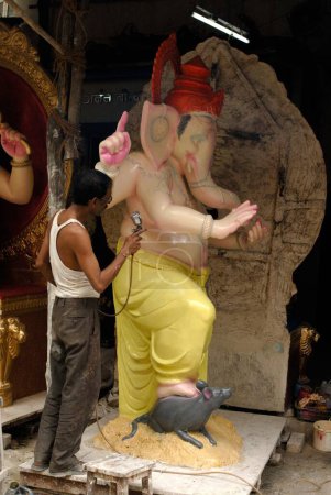 Photo for Man spray painting the big idol of lord Ganesh in Chitrashala ; Elephant headed god of Hindu ; Ganapati Festival at Lalbaug ; Bombay Mumbai ; Maharashtra ; India - Royalty Free Image