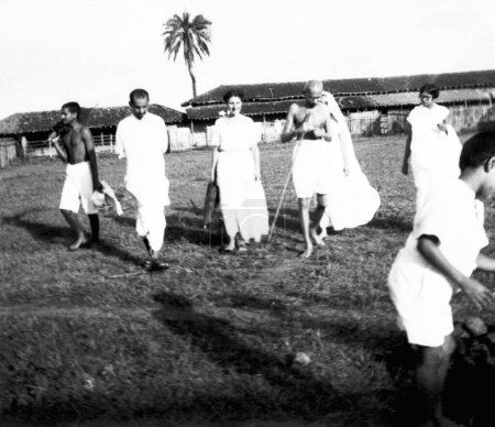 Foto de Mahatma Gandhi caminando con Hanna Lazar sobrina del Dr. Hermann Kallenbach, Shardabehn y otros en el Ashram Sevagram, 1938 - Imagen libre de derechos