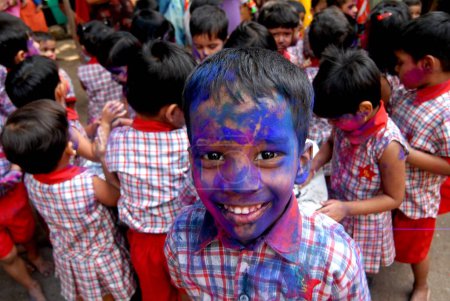 Foto de Los niños de la escuela celebran el festival de colores Holi mientras se aplican polvo de colores en las caras del otro en Bombay ahora Mumbai, Maharashtra, India - Imagen libre de derechos