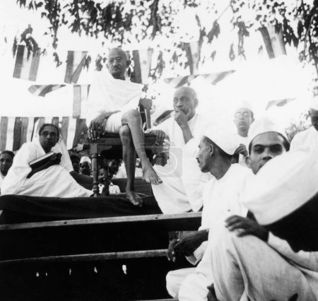 Téléchargez les photos : Mahatma Gandhi, assis sur une chaise, Sardar Vallabhbhai Patel et Pyarelal Nayar sur scène une réunion publique, 1940, Inde - en image libre de droit