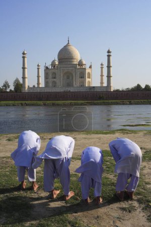 Téléchargez les photos : Jeunes garçons musulmans pratiquant la prière religieuse Namaz devant Taj Mahal Septième merveilles du monde sur la rive sud de la rivière Yamuna, Agra, Uttar Pradesh, Inde Site du patrimoine mondial de l'UNESCO - en image libre de droit