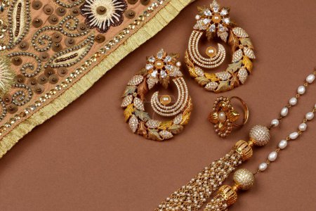 Téléchargez les photos : Bijoux de perles sur un fond brun, écharpe dorée, fond de bijoux de bracelet de perles, collier de perles, boucles d'oreilles en perles, bague de doigt. Style, mode et conception de bijoux. bijoux traditionnels indiens - en image libre de droit