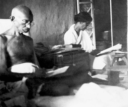 Téléchargez les photos : Mahatma Gandhi assis dans sa cabane à l'Ashram de Sevagram, 1938, à côté de lui Rajkumari Amrit Kaur - en image libre de droit