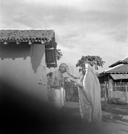 Téléchargez les photos : Mahatma Gandhi accueilli par une femme Parsi et présenté une noix de coco devant sa cabane à l'Ashram de Sevagram, janvier 1942 - en image libre de droit