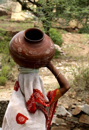 Foto de Mujer llevando agua en maceta de barro; ciudad de Dilwara; distrito de Rajasmand; Rajasthan; India - Imagen libre de derechos