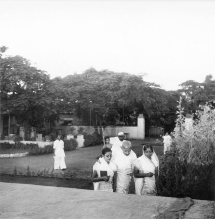 Foto de Abha Gandhi, Mahatma Gandhi y Kusumbehn Adani caminando por el complejo de la clínica de curación de la naturaleza en Pune, 1944 - Imagen libre de derechos