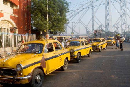 Photo for Taxi Stand and Howrah Bridge (Rabindra Setu)  A miracle of engineering skill  ; Huge cantilever and wide bridge ; Kolkata ; West Bengal ; India - Royalty Free Image