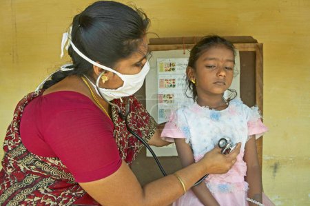 Téléchargez les photos : Travailleur de santé de l'ONG Chinmaya Organization of Rural Development CORD examinant la poitrine d'une fille malade avec stéthoscope au centre de santé, Siruvani, Karnataka, Inde - en image libre de droit