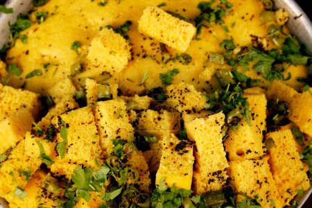 Snack indio llamado Khaman Dhokla hecho de masa de harina de gramo y cortado al horno en cuadrados con hojas de cilantro y trozos de chiles verdes esparcidos y servidos; Nathdwara; Rajasthan; India