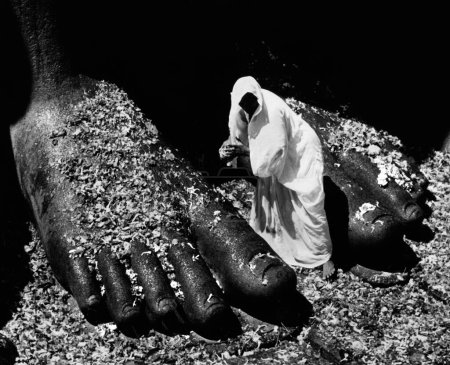 Téléchargez les photos : Femme pèlerin recueille les fleurs tombées des pieds gigantesques de la statue de granit de Gomatechvara ; à la fête mahamastakabhisheka (la grande onction) ; Sravanabelagola ; Karnataka ; Inde ; 1952 - en image libre de droit
