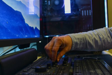 Photo for Hand of a white man in blue shirt playing mixing console in front of a blue monitor. - Royalty Free Image