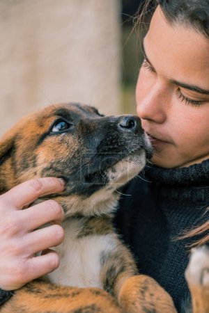 Primer plano de una joven veterinaria siendo cariñosa con un cachorro de perro en sus brazos.
