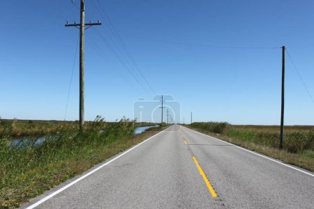 Scenic straight country road in the middle of nowhere in Texas on a sunny day in October. Canal and electric poles beside, yellow dividing road line. For rural, agricultural, and travel themes.