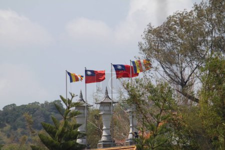 Two Taiwanese (Republic of China) flags and two buddhist flags waving between green trees at Fo guang shan monastery in Early Spring on a Cloudy day.