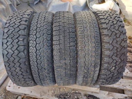 Four worn black tires, joined together, with four different tire treads or profiles. Pattern of grooves molded into rubber. Old used wheels stack together in garage. Tread pattern, texture, car equipment