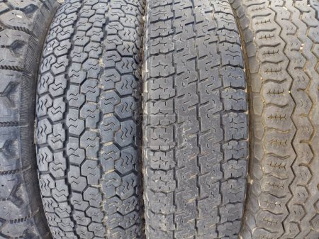 Close up of four worn black tires, joined together, with four different tire treads or profiles. Tread of tire refers to the rubber on its circumference that makes contact with road or ground.  Pattern of grooves molded into rubber