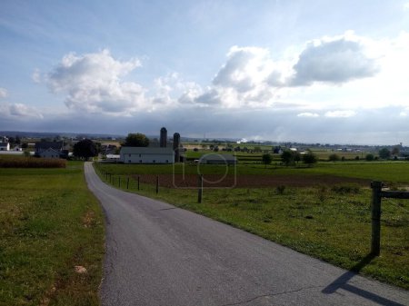 Foto de Condado de Lancaster, Estados Unidos, 5 de octubre de 2023: Escénica carretera rural en el país amish, con edificios agrícolas y tierras de cultivo en una tarde nublada en otoño, en el este de Pensilvania. - Imagen libre de derechos