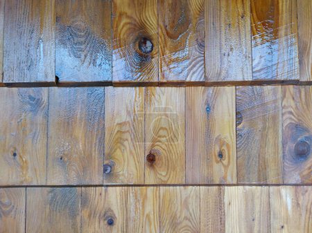 Primer plano de listones de pino, apilados en la pared exterior, agua corriendo hacia abajo. Fondo de madera brillante.