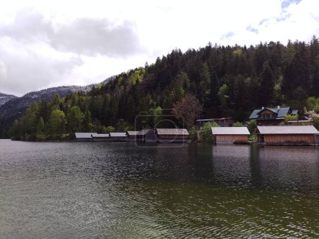 Beautiful traditional wooden boathouses at lake Altaussee in the Austrian Alps. Cloudy spring day. Green trees, snowy hills. Calming