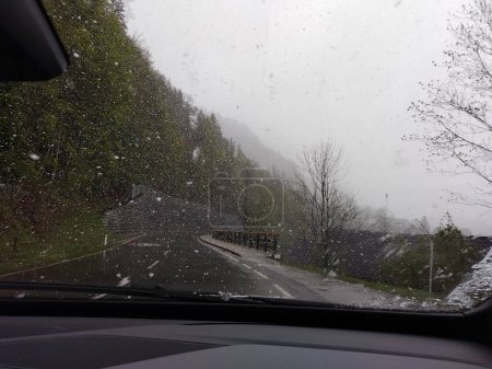 Photo for Driving carefully through snowstorm in spring in Austrian Alps, road trip. View out of window shield, passenger side. Snowing, road, bad sight, fog, bad weather, portentous mood. - Royalty Free Image