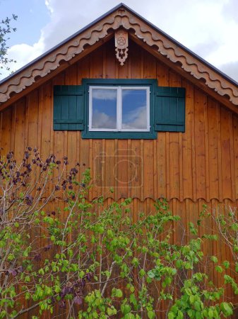 Schöne Holzfassade eines traditionellen österreichischen Hauses mit Holzdetails und grünen Fensterbänken in der Bergstadt Altaussee, in den Alpen. Bewölkter Tag im Frühling. Grüne Blätter im Vordergrund. Haustüren.