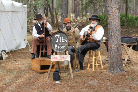 Photo for Olustee, Florida, USA - February 16, 2020: Band 7 lbs of bacon perfoms at Olustee Re-enactment in Florida 2020. Musicians playing authentical music in traditional clothing. Southern. Civil war era. Three musicians with hats and beards. Nostalgia - Royalty Free Image