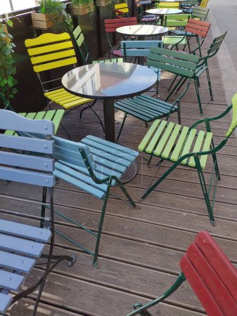 Bunte Sitzecke im Freien. Vintage gestylte leere Gastgarten. Außentische und robuste Stühle vor einer geschlossenen Kneipe in der Wiener Innenstadt. Einladende Anordnung auf Holzplattform