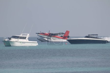 Foto de Kuredu, Maldivas, 9 de diciembre de 2014: hidroavión Trans Maldivas Airways en movimiento entre barcos de lujo en el Océano Índico. Vista lateral. Turbohélice, de color rojo blanco. Doble nutria hidroavión y yate - Imagen libre de derechos