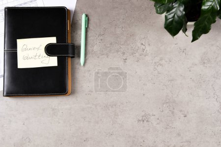 Photo for Workplace desk with paper business notebook planner with sticky note and text Quiet Quitting on it. Work-to-rule, in which employees engage in work related activities solely within defined work hours. - Royalty Free Image