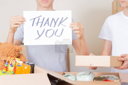 Photo for Thank you for donation. Volunteers collecting donations for charity. Teenagers holding paper sheet with message Thank you over cardboard boxes full of food glocery, clothes, toys. - Royalty Free Image