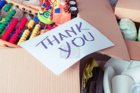 Photo for Donations boxes with kid toys, clothes, dishes, household items, grocery products and paper card with inscription Thank you. Donation, charity, food bank, help for poor, low income families. - Royalty Free Image